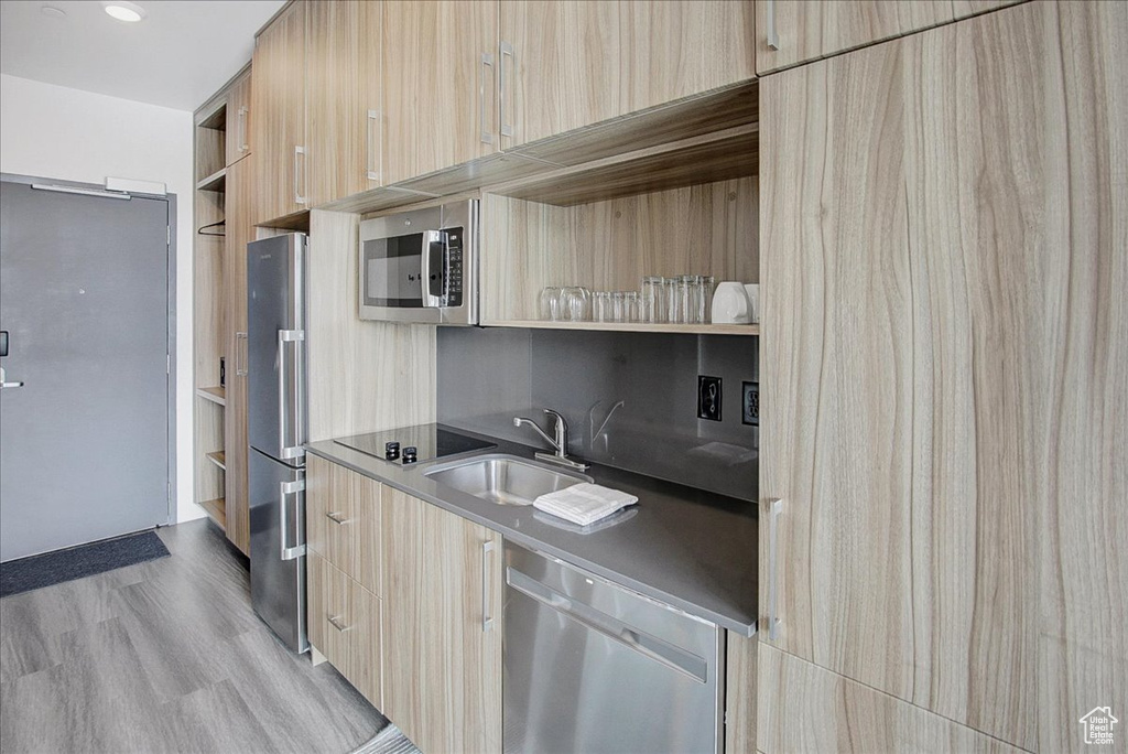 Kitchen with appliances with stainless steel finishes, light brown cabinets, sink, and light wood-type flooring