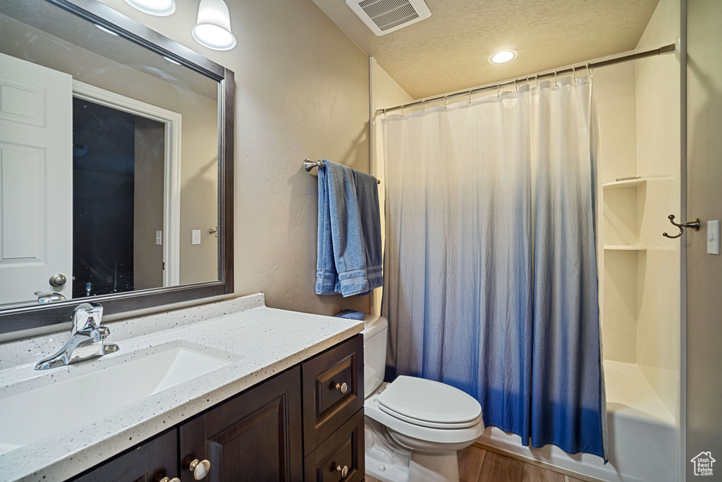Full bathroom with toilet, a textured ceiling, vanity, and shower / bath combo with shower curtain