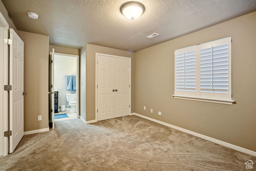 Unfurnished bedroom featuring a closet, a textured ceiling, and light colored carpet
