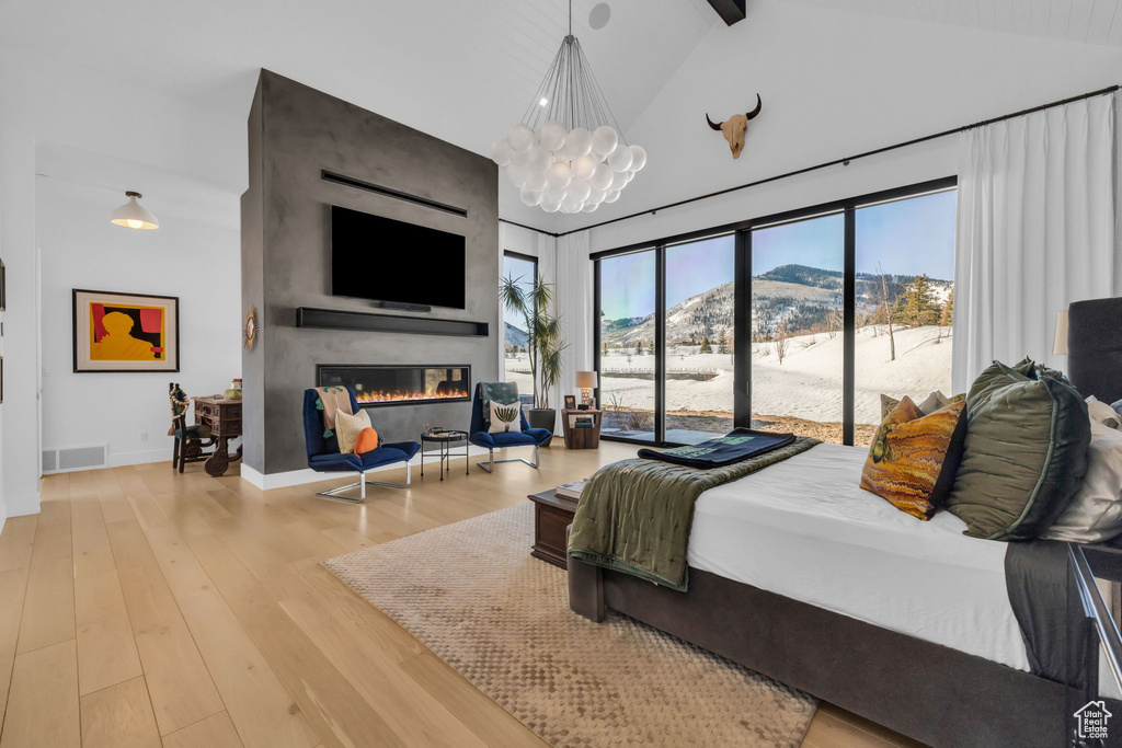 Bedroom with a notable chandelier, a large fireplace, light hardwood / wood-style floors, a mountain view, and high vaulted ceiling