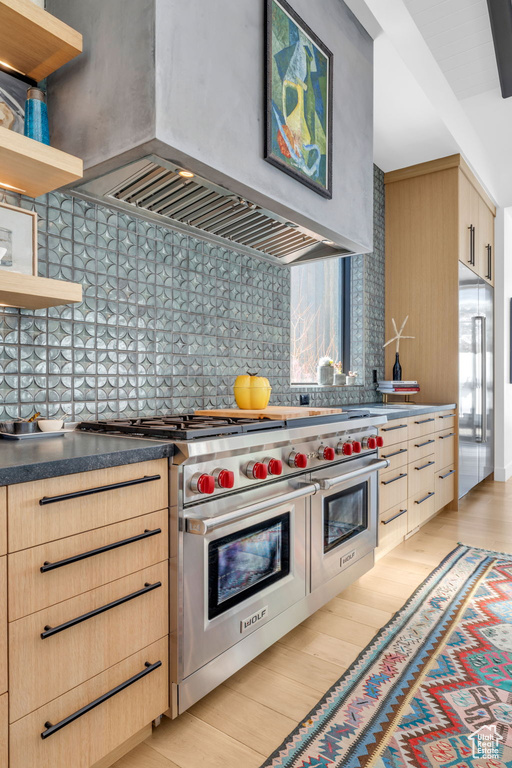 Kitchen featuring backsplash, light brown cabinets, light hardwood / wood-style flooring, custom range hood, and range with two ovens