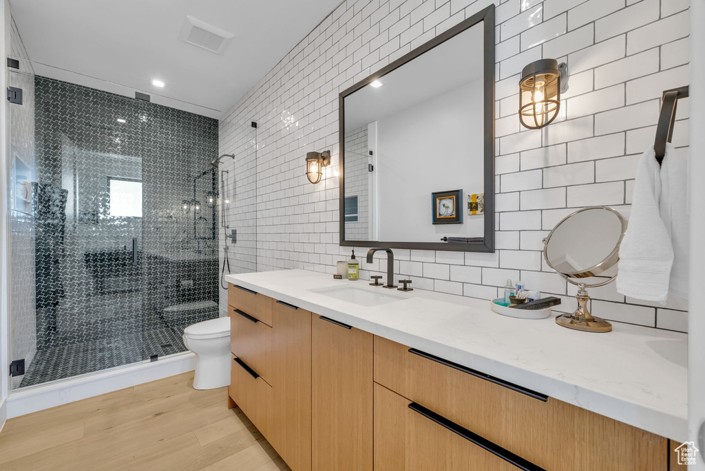Bathroom with tile walls, wood-type flooring, a shower with door, toilet, and oversized vanity