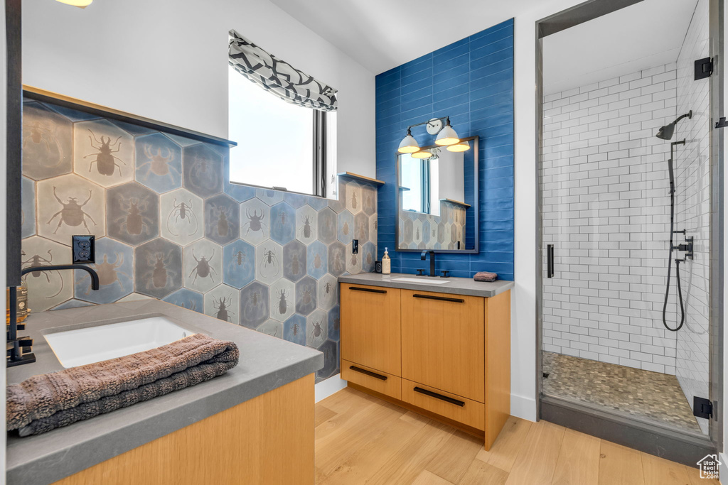 Bathroom featuring wood-type flooring, tile walls, walk in shower, and vanity
