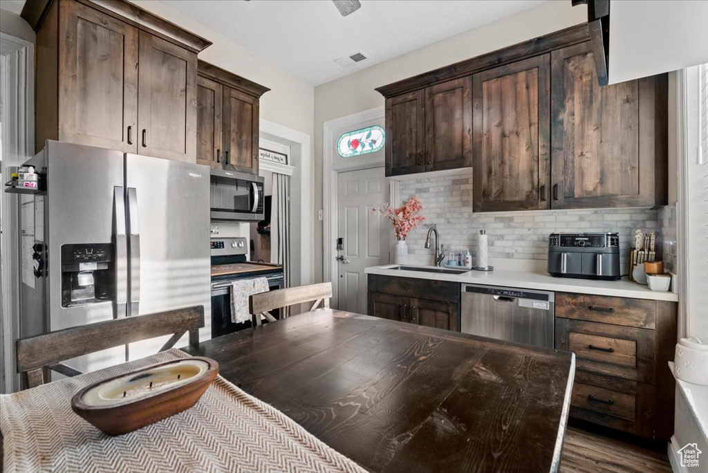 Kitchen with tasteful backsplash, wood-type flooring, appliances with stainless steel finishes, and dark brown cabinets