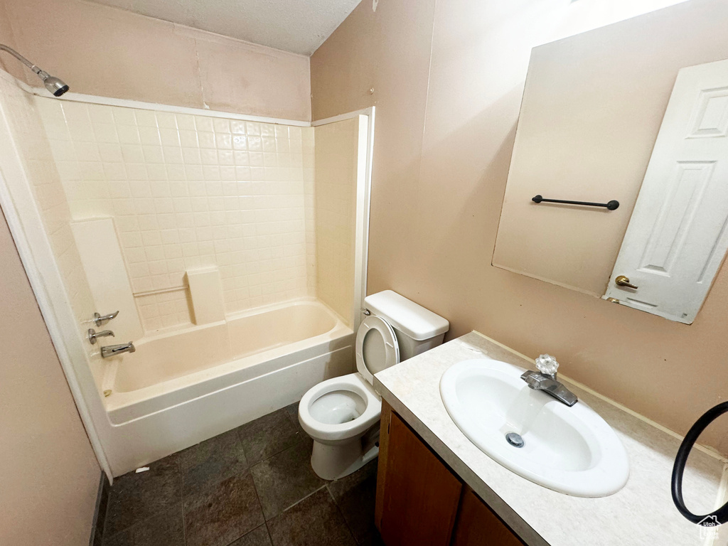 Full bathroom with tile floors, vanity with extensive cabinet space, toilet, and tiled shower / bath