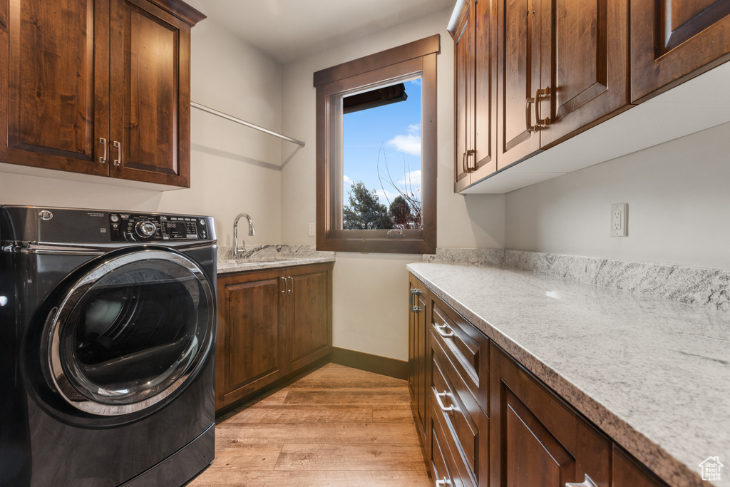 Clothes washing area with cabinets, washer / dryer, sink, and light hardwood / wood-style flooring