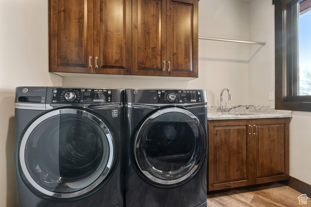 Laundry area with light hardwood / wood-style floors, washer and clothes dryer, cabinets, and sink