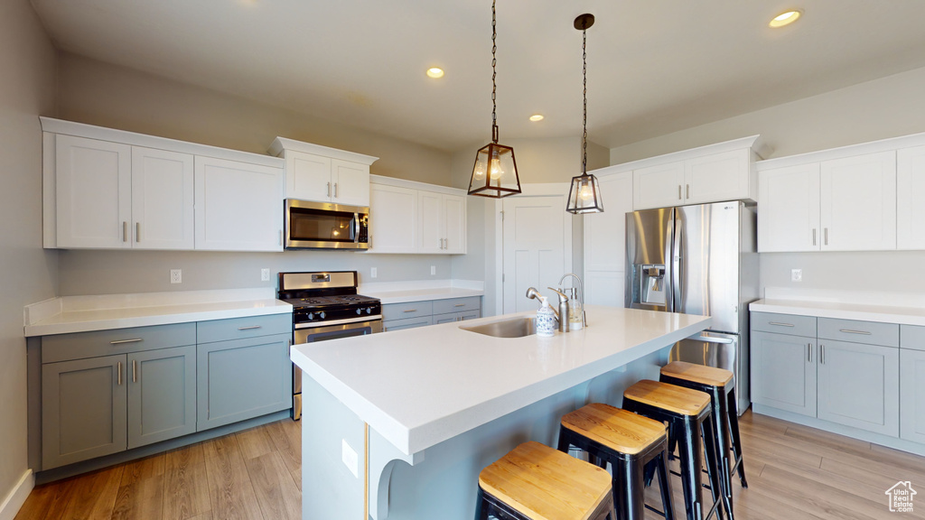 Kitchen featuring sink, light hardwood / wood-style floors, appliances with stainless steel finishes, a kitchen island with sink, and decorative light fixtures