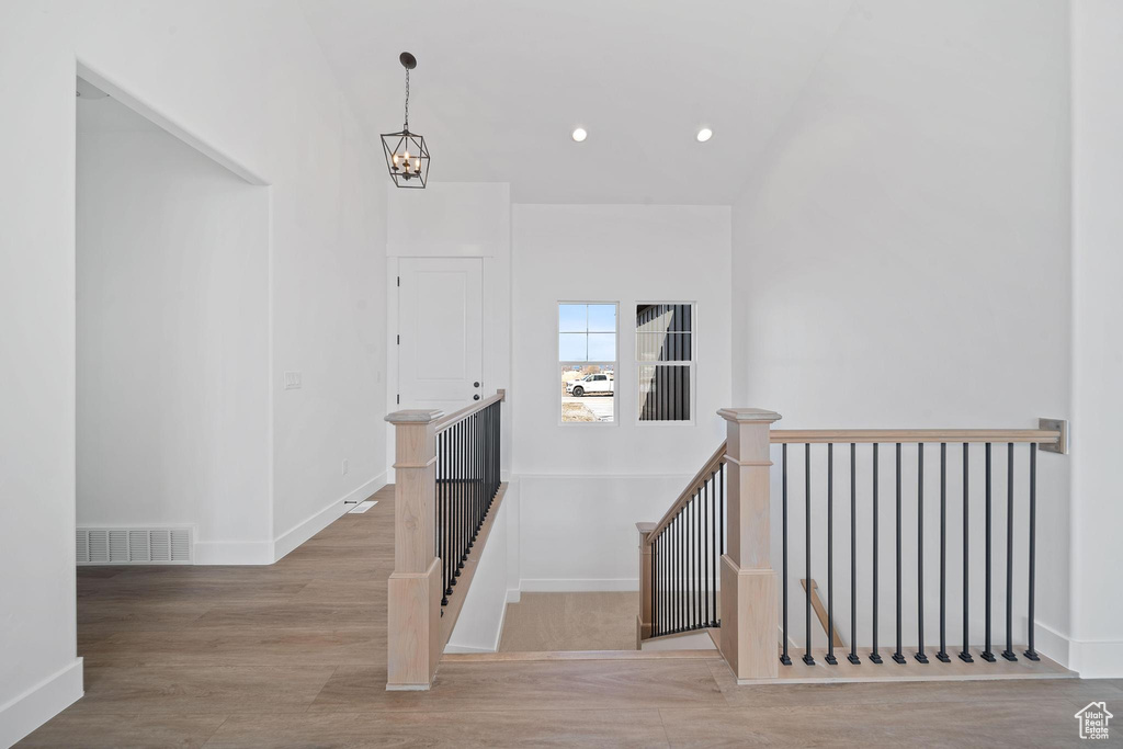 Stairway featuring an inviting chandelier, vaulted ceiling, and light hardwood / wood-style flooring