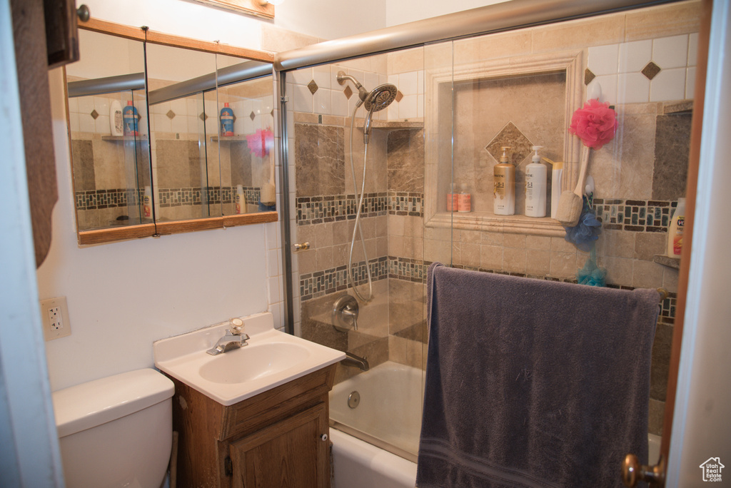 Full bathroom with toilet, shower / bath combination with glass door, oversized vanity, and tile walls