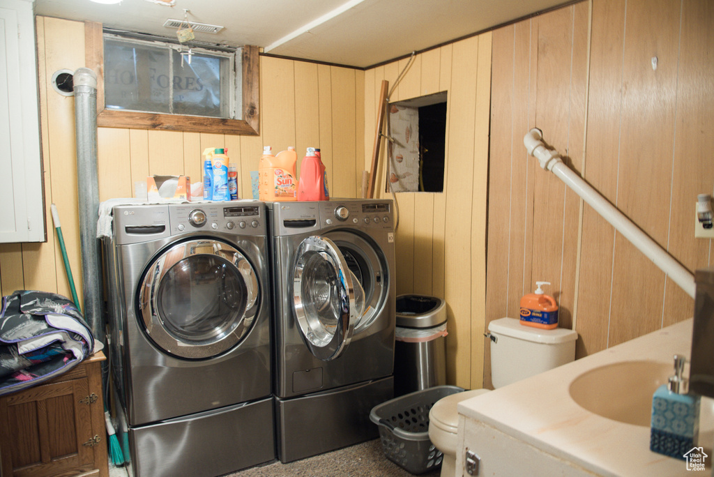 Clothes washing area featuring wood walls, separate washer and dryer, and sink