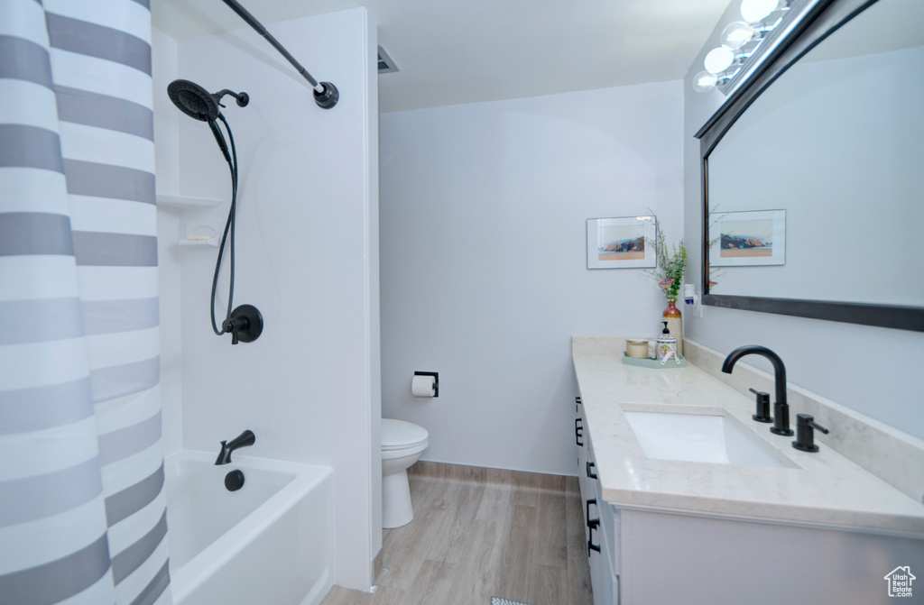 Full bathroom featuring toilet, shower / tub combo, vanity with extensive cabinet space, and hardwood / wood-style flooring
