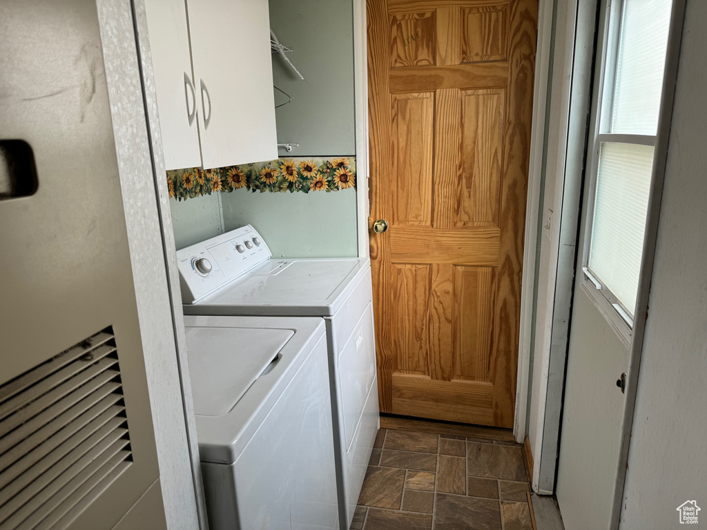 Clothes washing area with separate washer and dryer, dark tile flooring, cabinets, and a wealth of natural light