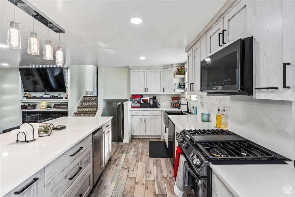 Kitchen with hanging light fixtures, backsplash, appliances with stainless steel finishes, sink, and light wood-type flooring