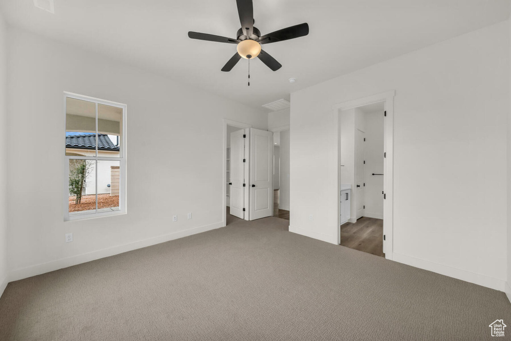Unfurnished bedroom with connected bathroom, ceiling fan, and dark colored carpet