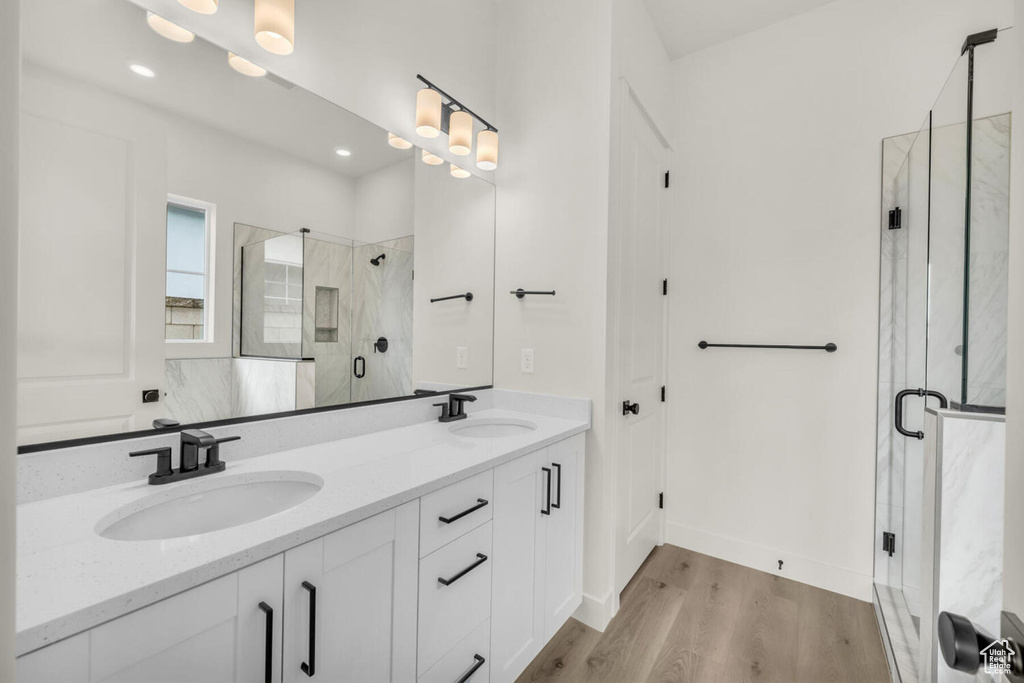 Bathroom featuring hardwood / wood-style floors, a shower with door, and dual bowl vanity