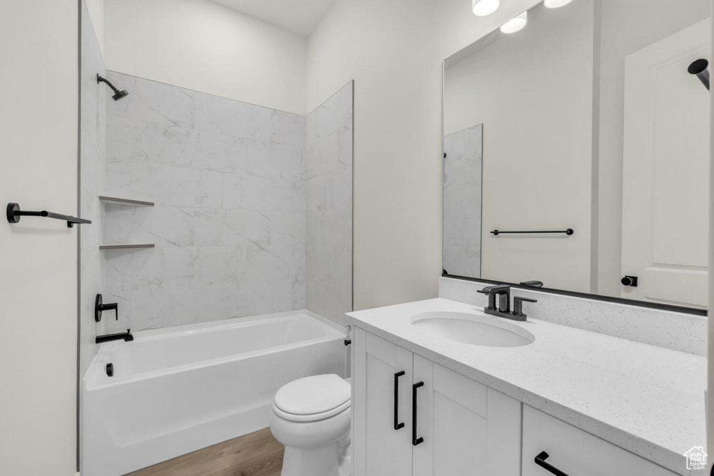 Full bathroom featuring tiled shower / bath combo, toilet, large vanity, and hardwood / wood-style flooring
