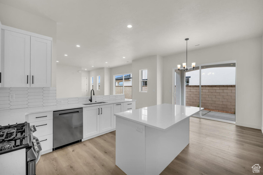 Kitchen featuring appliances with stainless steel finishes, a notable chandelier, sink, light wood-type flooring, and white cabinets