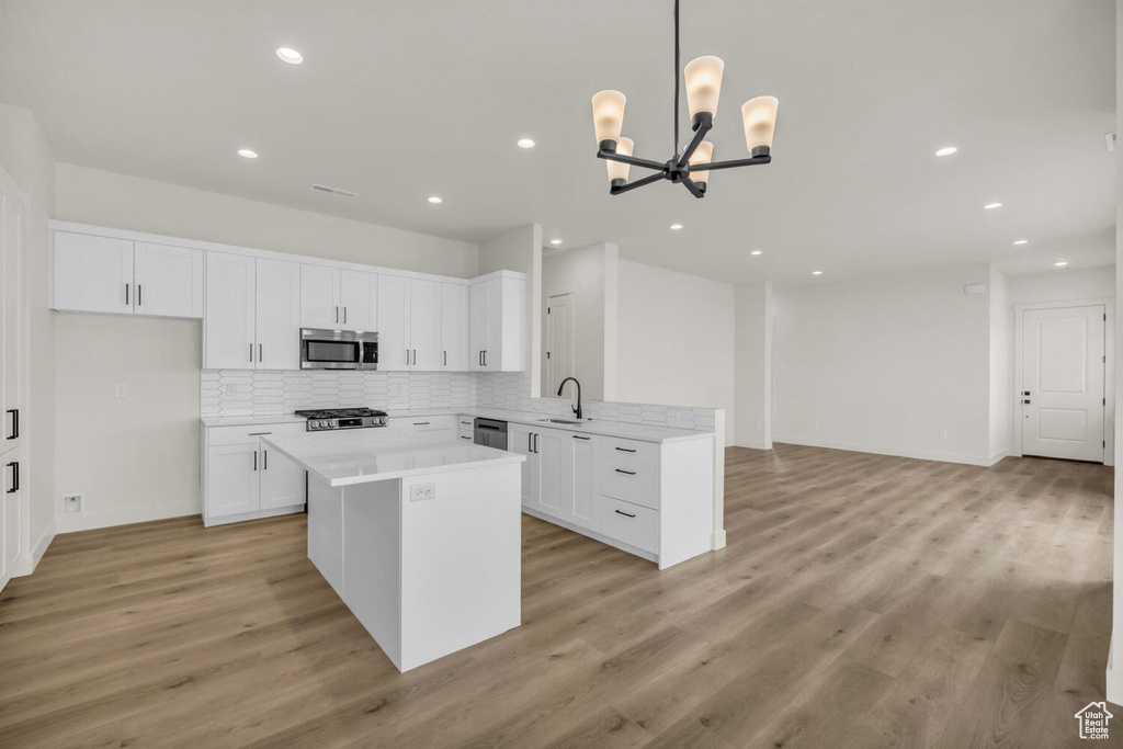 Kitchen with an inviting chandelier, appliances with stainless steel finishes, light hardwood / wood-style flooring, white cabinets, and pendant lighting