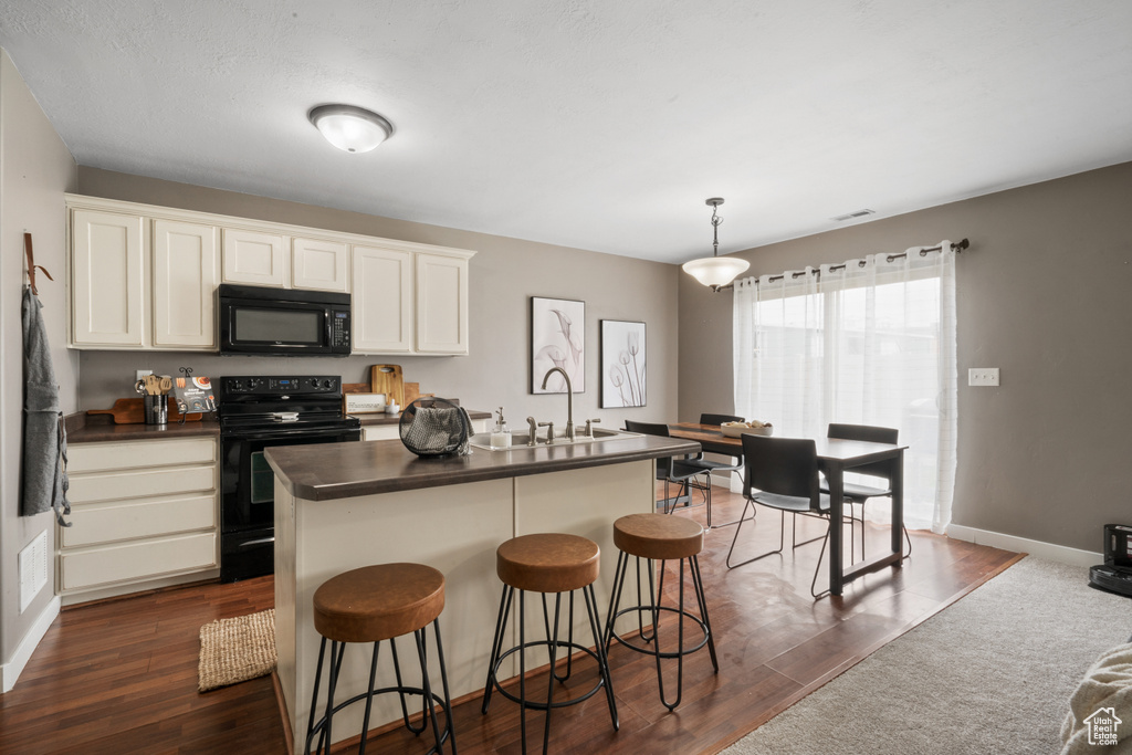 Kitchen featuring hanging light fixtures, dark wood-type flooring, black appliances, sink, and an island with sink