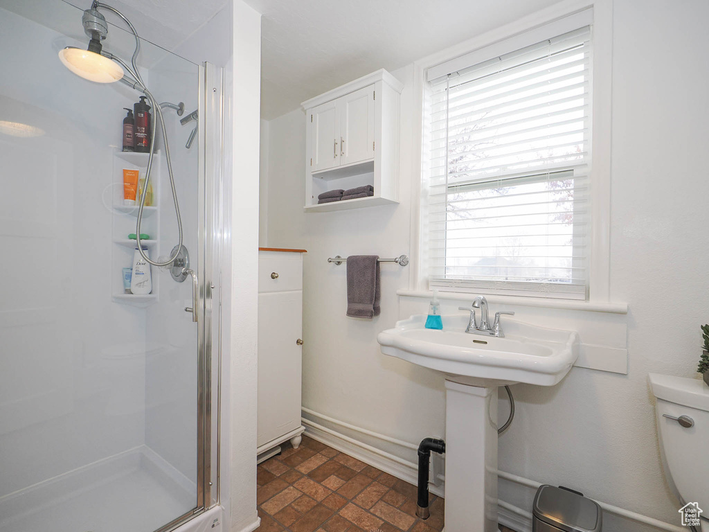 Bathroom featuring a shower with door, tile flooring, toilet, and a wealth of natural light
