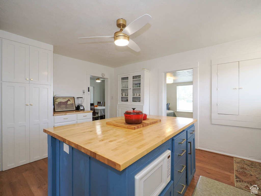 Kitchen featuring blue cabinets, a kitchen island, white microwave, wood counters, and dark wood-type flooring