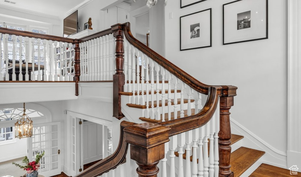 Staircase with crown molding, an inviting chandelier, and hardwood / wood-style floors