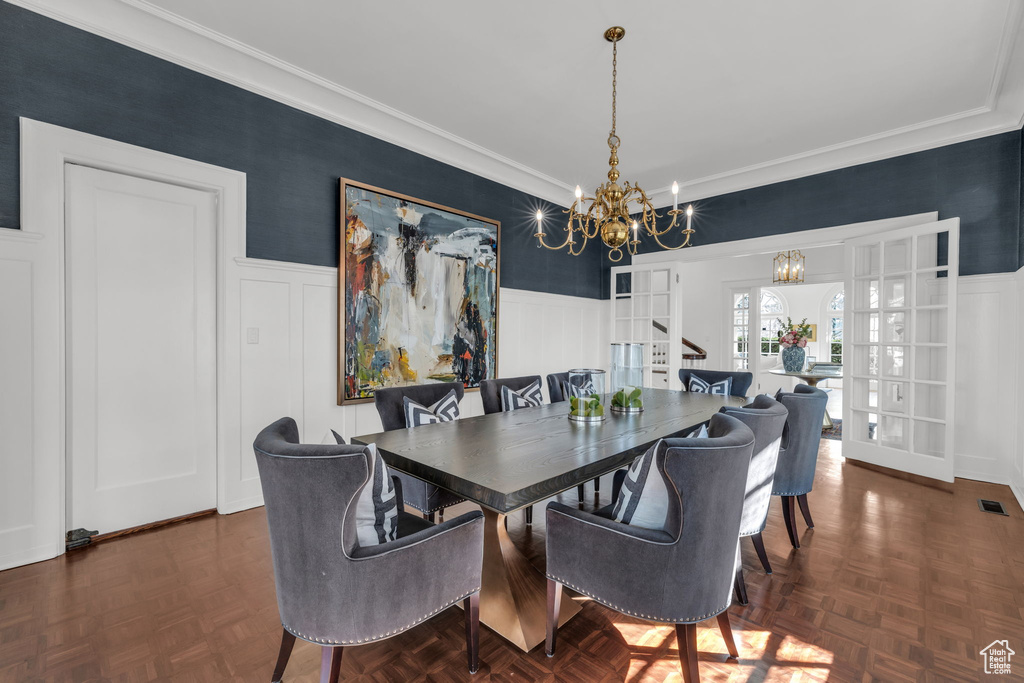 Dining space featuring dark parquet floors, a chandelier, french doors, and ornamental molding