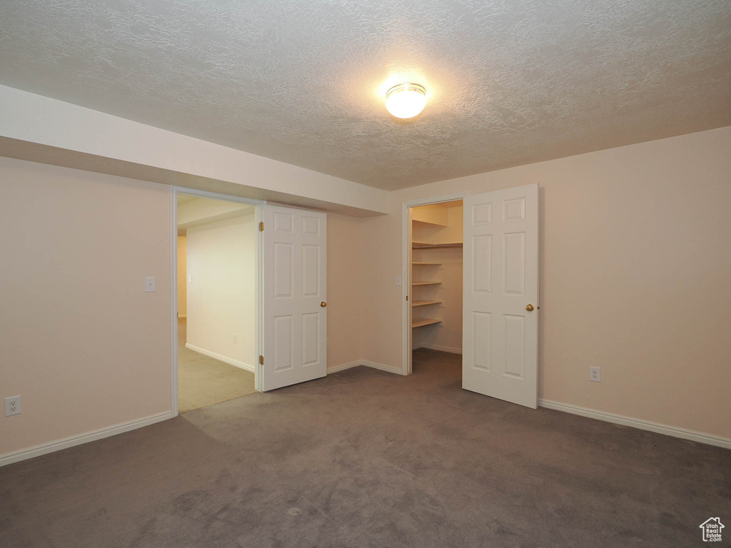 Unfurnished bedroom featuring a closet, a spacious closet, a textured ceiling, and dark colored carpet