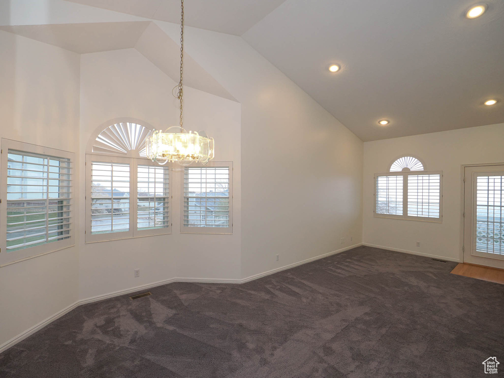 Empty room with an inviting chandelier, dark carpet, and high vaulted ceiling