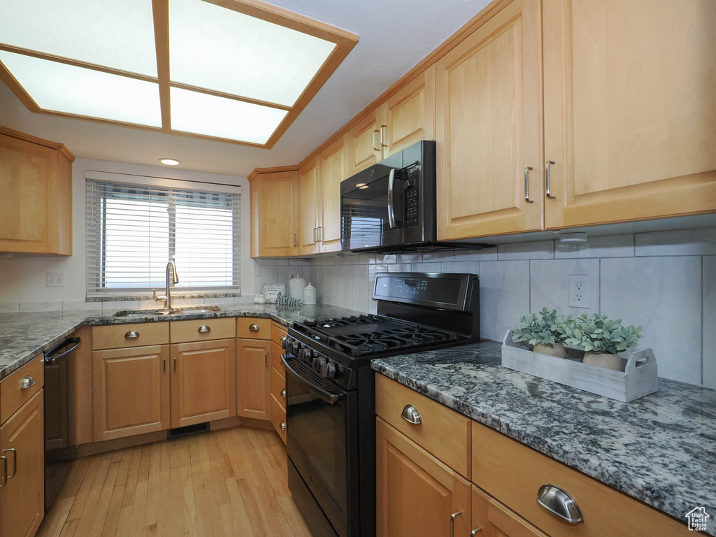Kitchen with backsplash, black appliances, light hardwood / wood-style floors, sink, and dark stone countertops