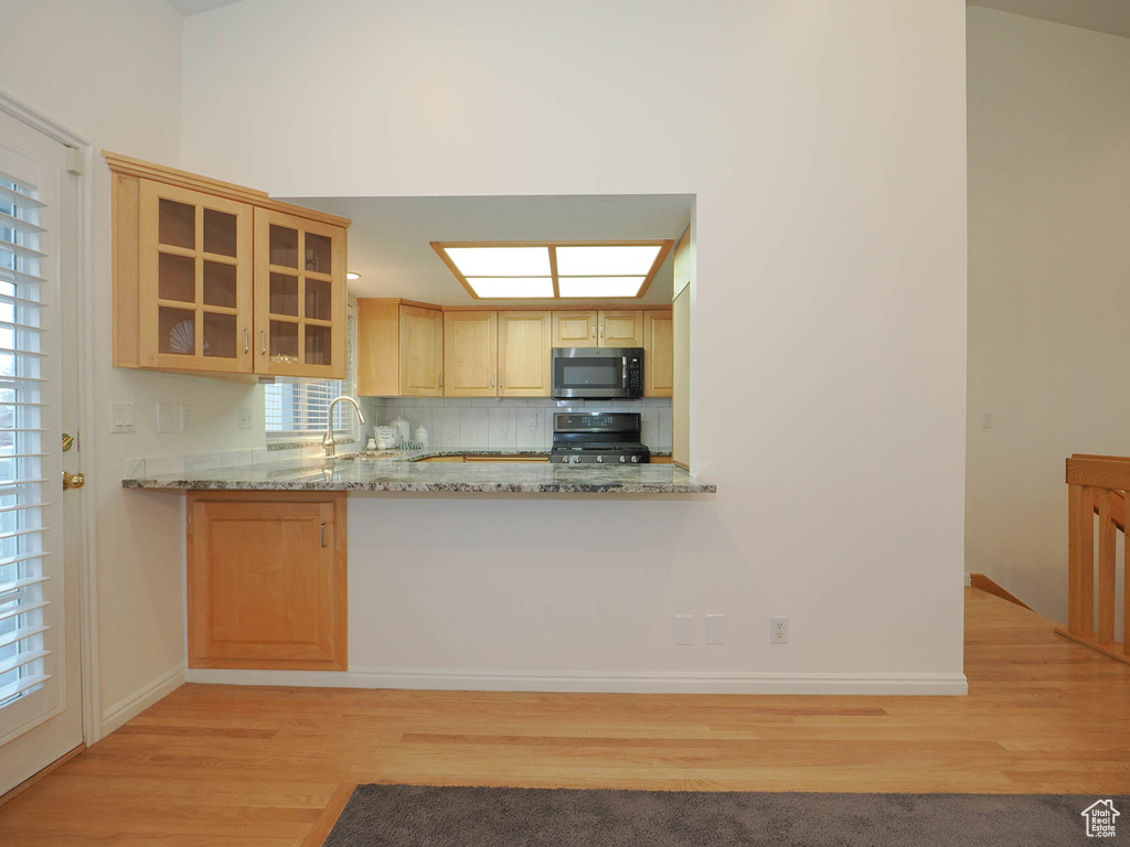 Kitchen with stove, light stone counters, tasteful backsplash, and light hardwood / wood-style flooring
