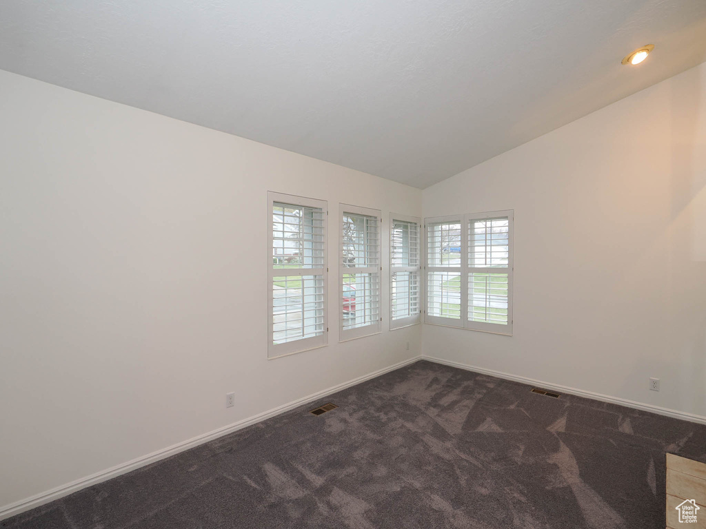 Empty room with dark carpet and vaulted ceiling