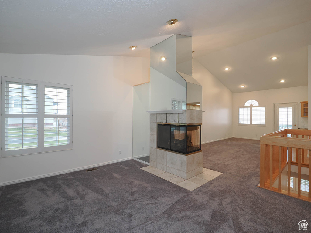 Unfurnished living room featuring lofted ceiling, dark carpet, and a tile fireplace
