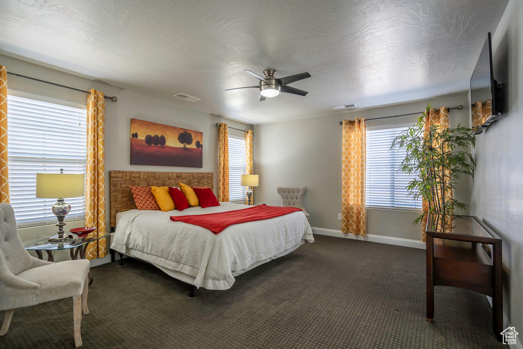 Bedroom with dark colored carpet, ceiling fan, and multiple windows