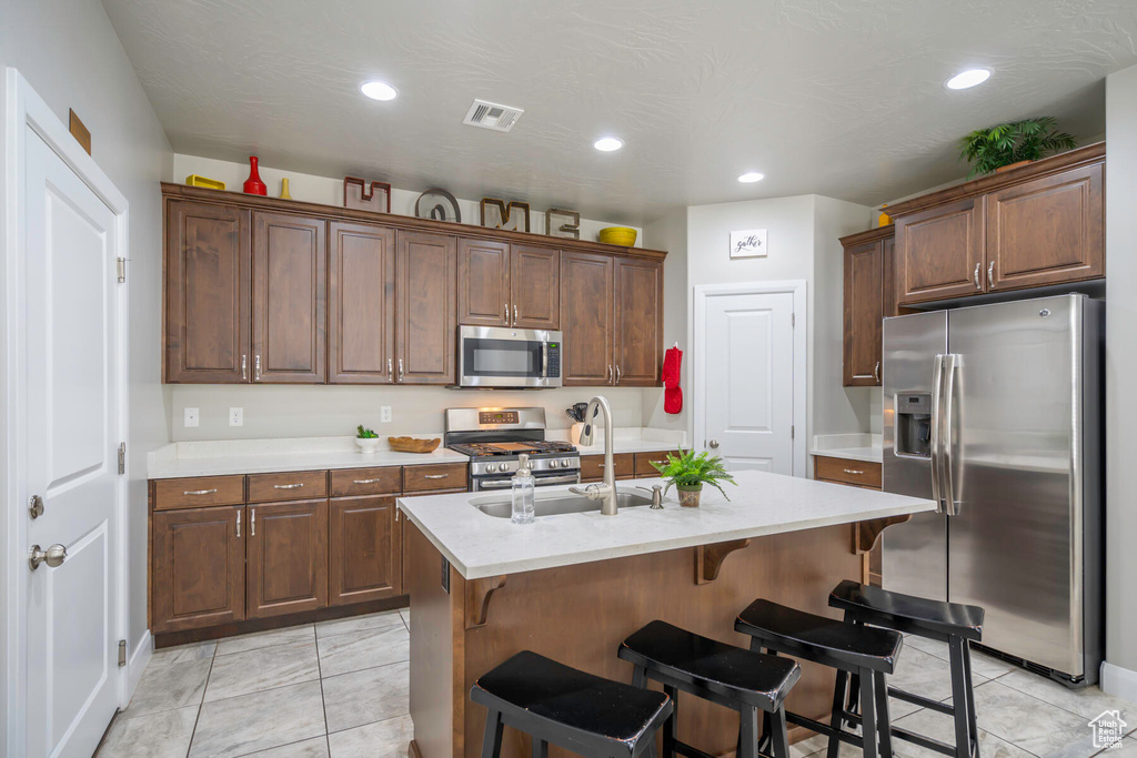 Kitchen with light tile floors, stainless steel appliances, a kitchen island with sink, sink, and a breakfast bar