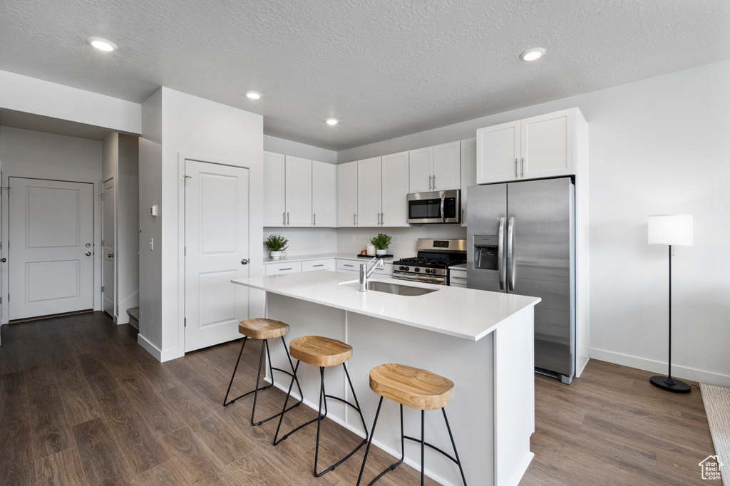 Kitchen featuring a kitchen breakfast bar, appliances with stainless steel finishes, white cabinets, a center island with sink, and dark hardwood / wood-style flooring
