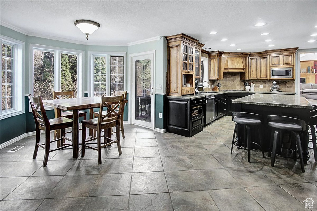 Kitchen with light stone counters, a breakfast bar area, stainless steel appliances, backsplash, and ornamental molding