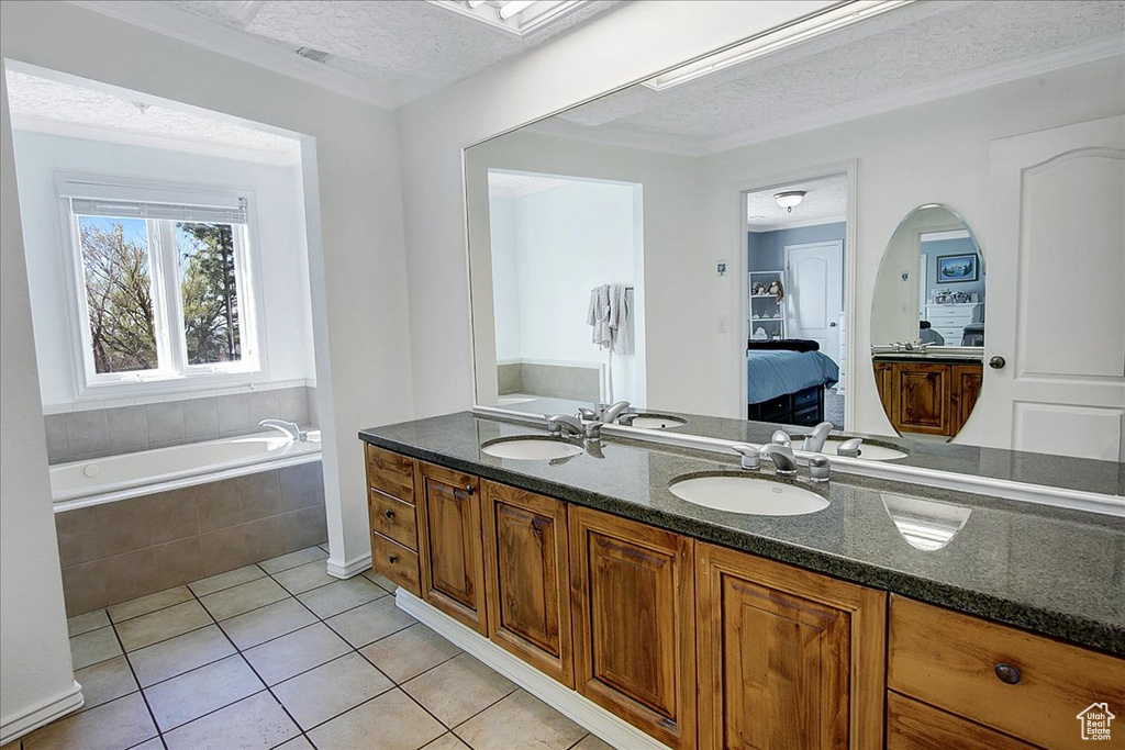 Bathroom with vanity with extensive cabinet space, tiled bath, tile floors, dual sinks, and a textured ceiling