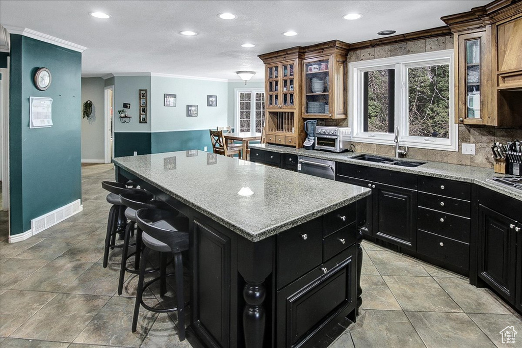 Kitchen featuring light tile floors, a center island, tasteful backsplash, ornamental molding, and sink