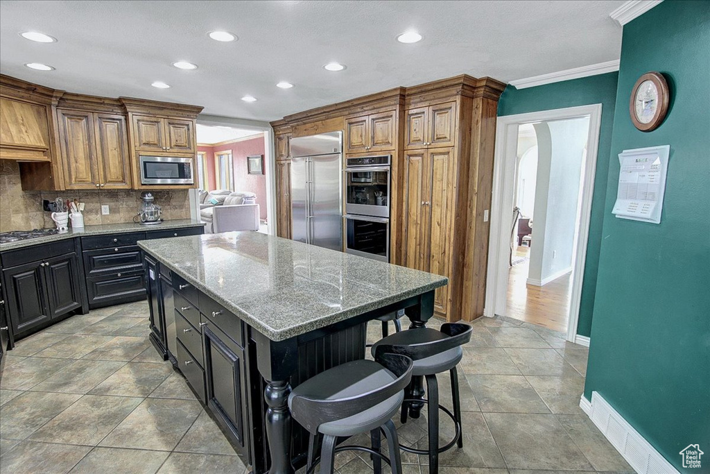 Kitchen with tasteful backsplash, a center island, light tile floors, built in appliances, and crown molding