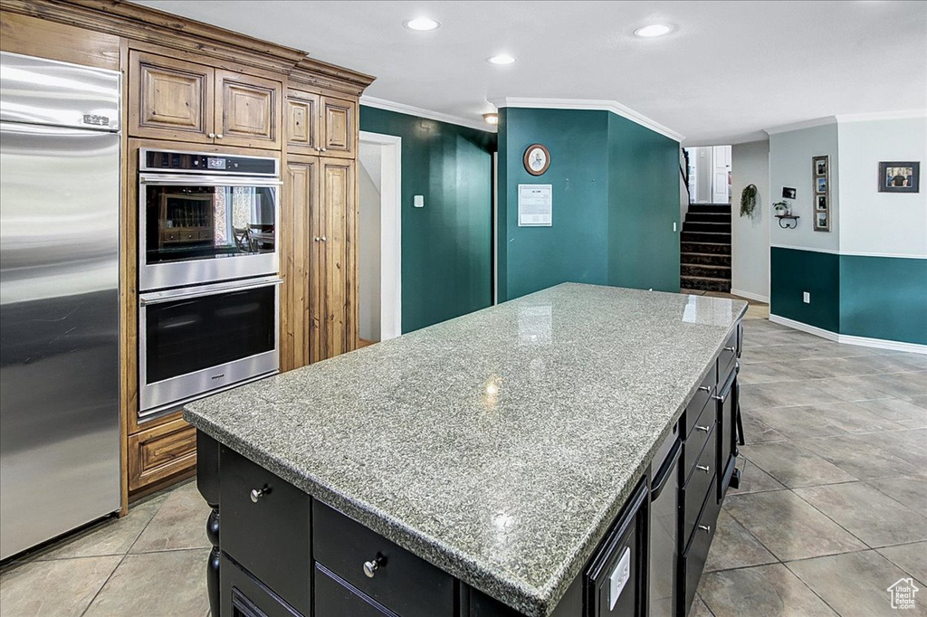 Kitchen featuring appliances with stainless steel finishes, light stone counters, a center island, ornamental molding, and light tile flooring