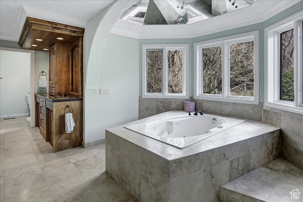 Bathroom featuring a relaxing tiled bath, crown molding, tile flooring, a textured ceiling, and vanity