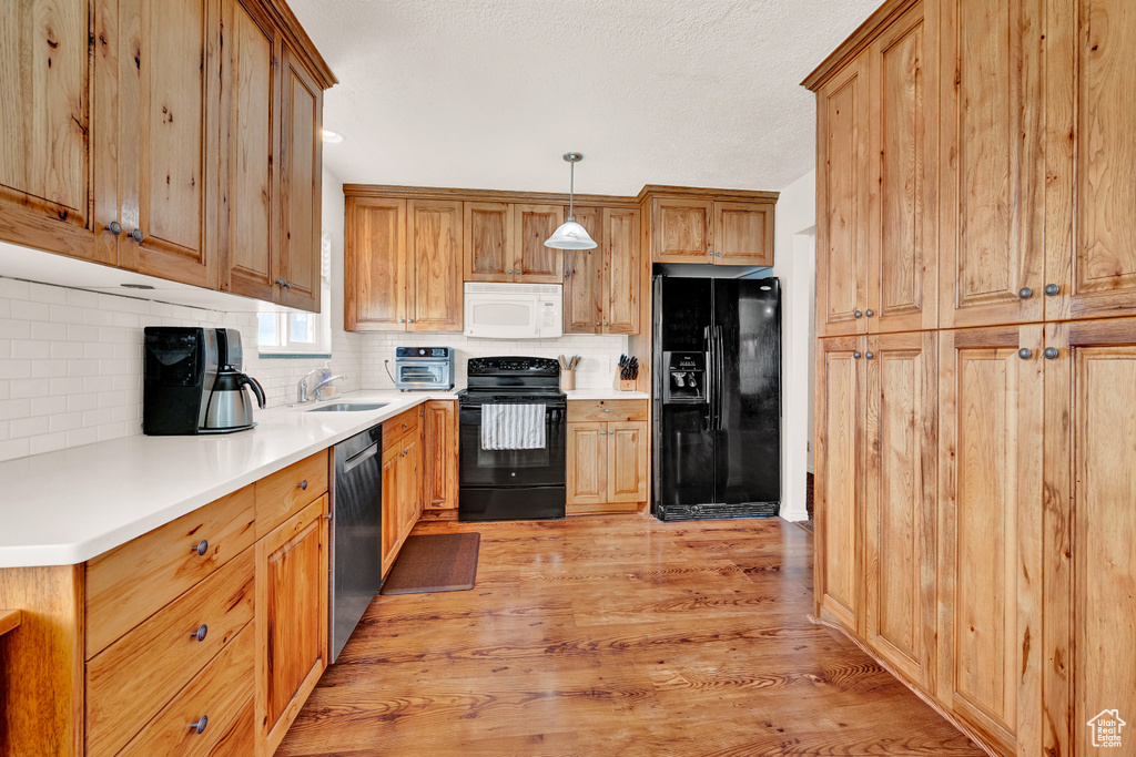 Kitchen featuring pendant lighting, light hardwood / wood-style floors, tasteful backsplash, black appliances, and sink