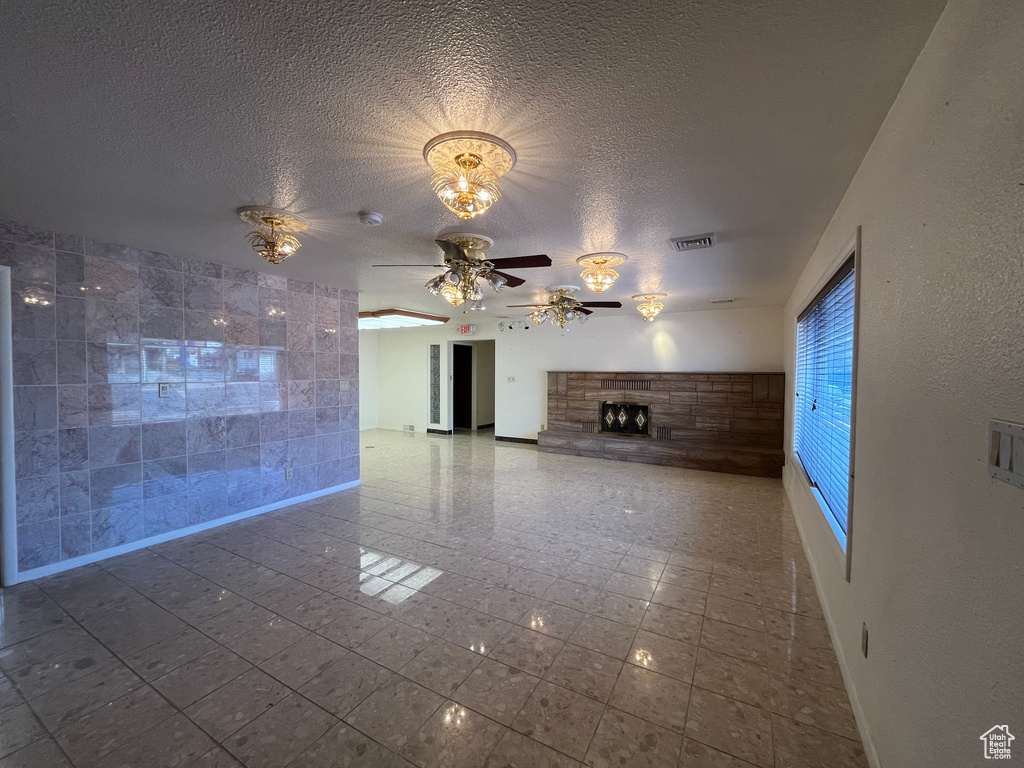 Unfurnished living room with a fireplace, tile flooring, a textured ceiling, and ceiling fan with notable chandelier