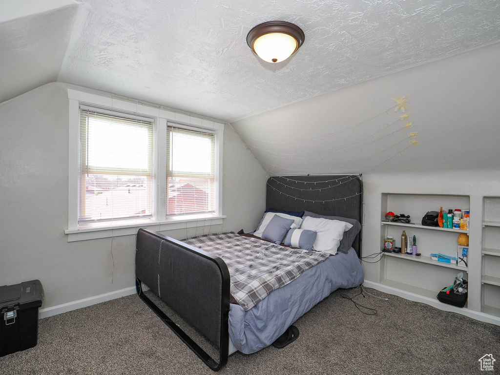 Bedroom with vaulted ceiling, dark carpet, and a textured ceiling