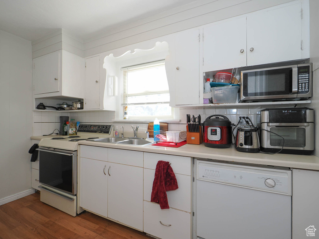 Kitchen featuring hardwood / wood-style floors, sink, tasteful backsplash, white appliances, and white cabinetry