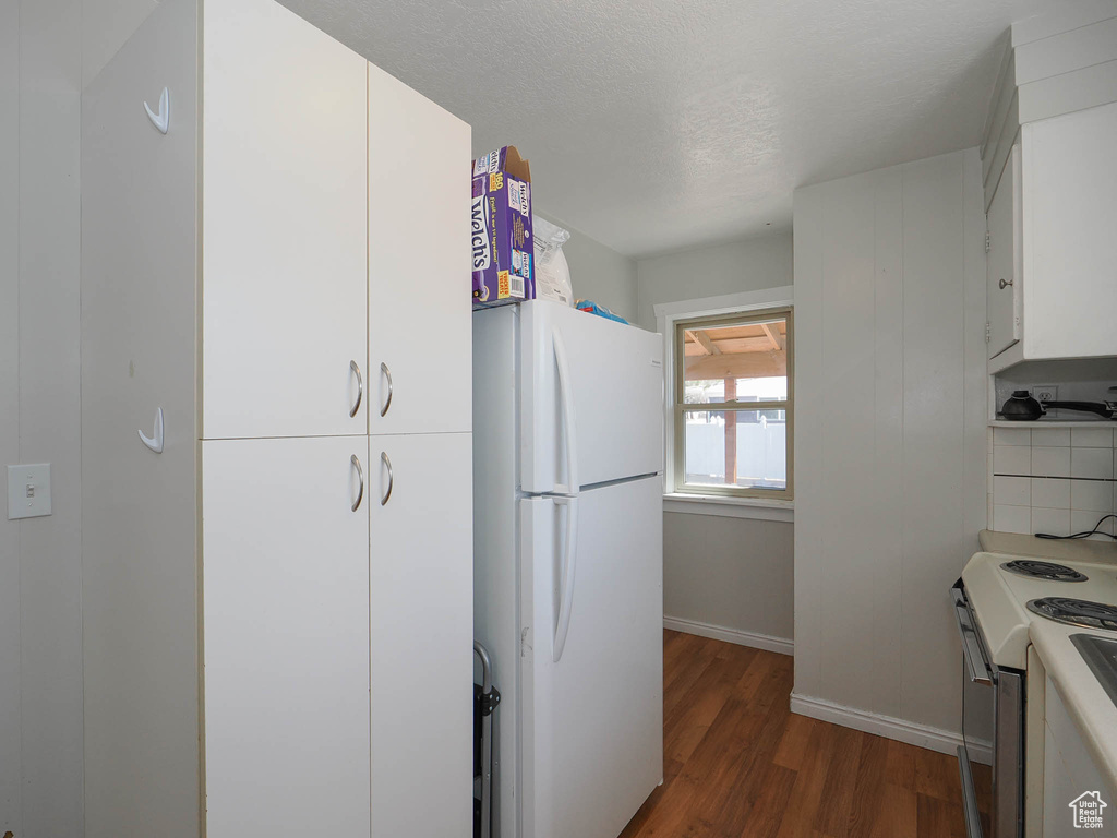 Kitchen with tasteful backsplash, white cabinets, white appliances, and dark hardwood / wood-style floors