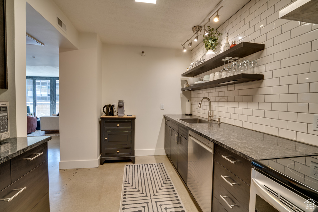 Kitchen featuring sink, rail lighting, dark stone countertops, dishwasher, and tasteful backsplash
