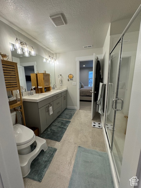 Bathroom with toilet, a textured ceiling, a shower with shower door, and dual vanity